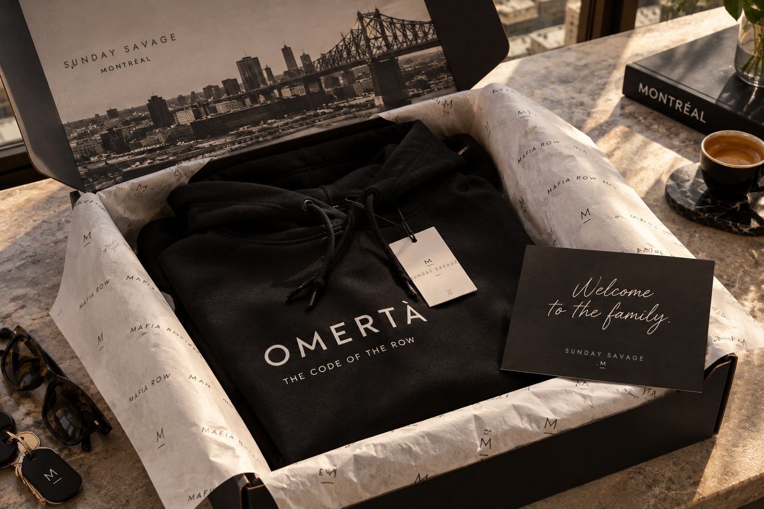 An Omertà hoodie in a black Sunday Savage box with tissue paper and a card that reads Welcome to the family